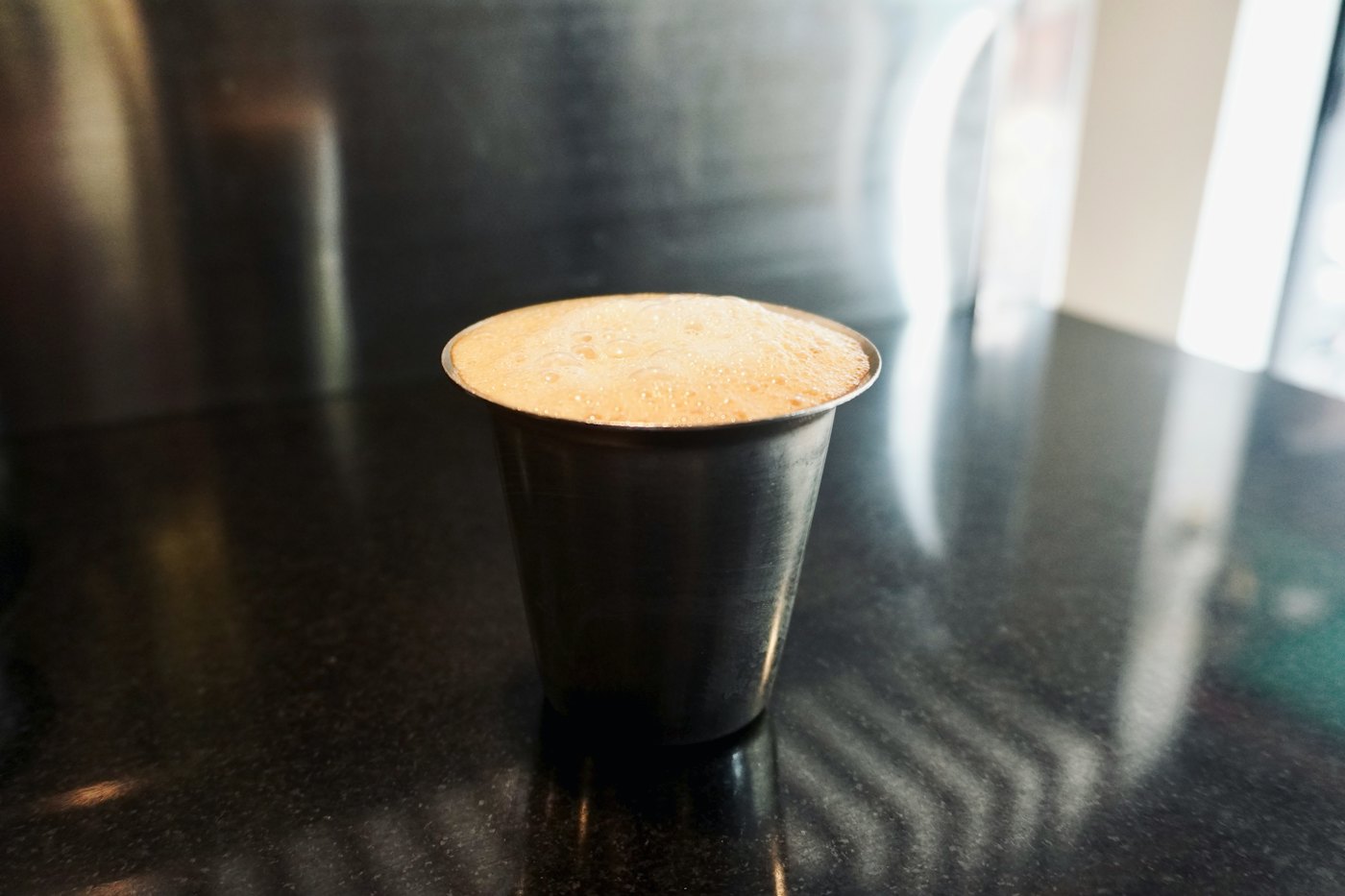 A frothy filter coffee in a steel tumbler on a dark counter
